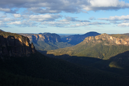 A landscape picture of mountains clad with forest below a cloudy blue sky の写真素材