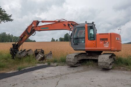 Katrineholm, Sweden -  July  28, 2017: Orange  Excavator  parked by the road partly in a fieldのeditorial素材