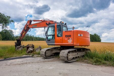 Katrineholm, Sweden -  July  22, 2017: Orange  Excavator  parked by the road partly in a fieldのeditorial素材