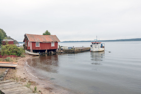 Norrkoping, Sweden-September 23, 2017: Old fishing boat at the harbour in Kvarsebo, with a red house next to it.のeditorial素材