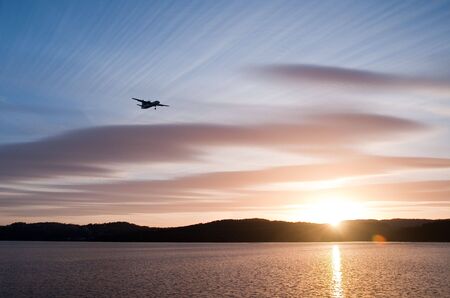 Airplane in the sunset over the water with blue sky and hills in the backgroundの写真素材