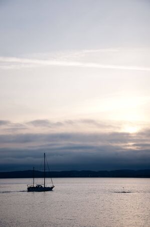 Sailboat in dark sunset with hills in the backgroundの写真素材
