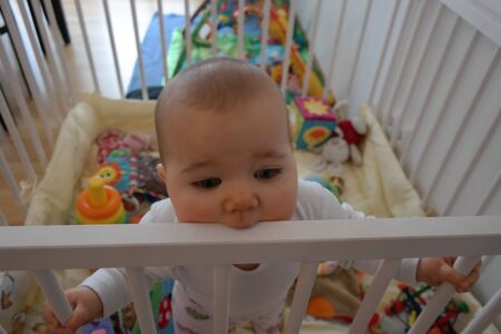 Baby steht in Laufstall und beusst in Gitterの写真素材