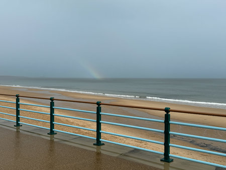 Retro seaside mint coloured handrail at walkway or promenade at the beach with golden beach and waves in Whitley bay, Newcastle, England. Faint rainbow at seaの写真素材