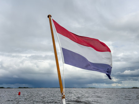 Waving Dutch flag, red, white and blue in wind or storm at a sailing boat in Friesland on al lake with dark, storm cloudsの写真素材