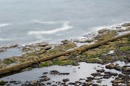 Long exposure of granite stone pier seawall and rocks along coast coastline in England, UK,...