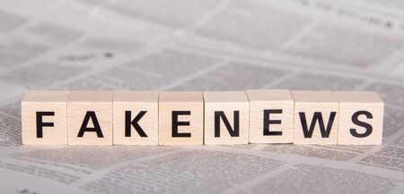 fakenews text on wooden cubes, newspaper as backgroundの写真素材