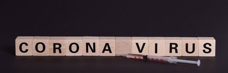 wooden cubes with text coronavirus and a syringe, vaccine, black backgroundの写真素材