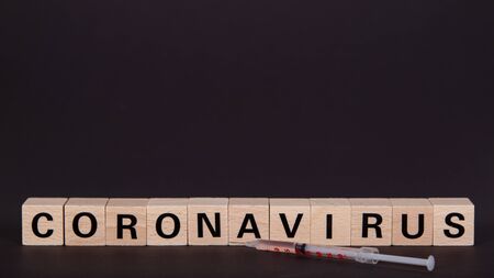wooden cubes with text coronavirus and a syringe, vaccine, black backgroundの写真素材