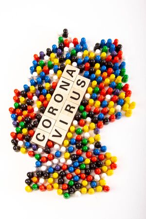 Map of Germany with text corona virus in the middle, in several colors representing all nationalities that life in Germany, build with wooden figurines, white backgroundの写真素材