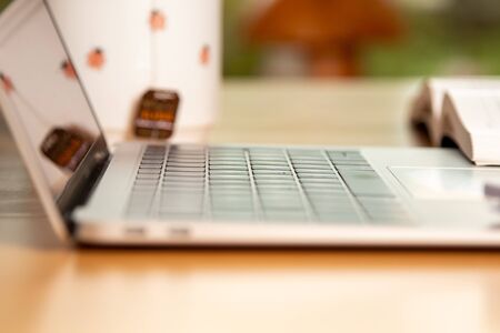 side view on a laptop, tea cup and open book in the background