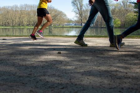 legs of a jogger and walking peolpe in a park, lake as background, sunny day