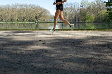 legs of a jogger in a park, lake as background, sunny dayの写真素材