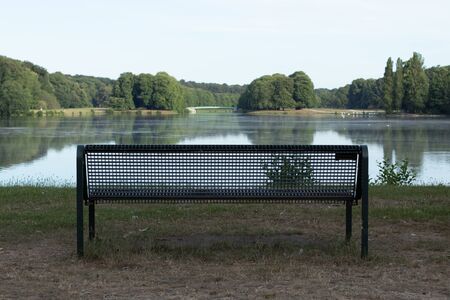 empty bench in a park with a nice view on a lake, blurred background, cloudy skyの写真素材