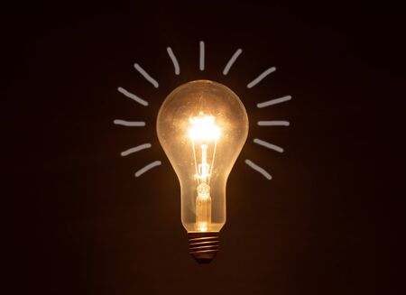 glowing light bulb against dark background, drawn stripes as rays of light, copy spaceの写真素材