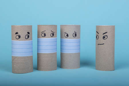 four empty toilet paper rolls, three with face mask looking to one without mouth protection, blue backgroundの写真素材