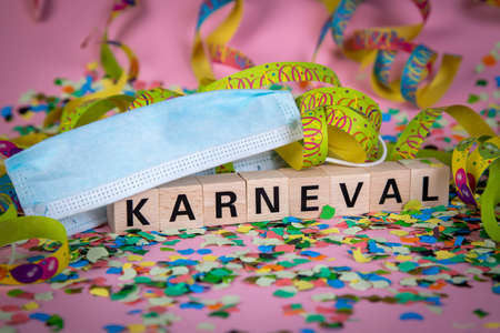 German word KARNIVAL on wooden blocks under a face mask with confetti and streamers, pink backgroundの写真素材