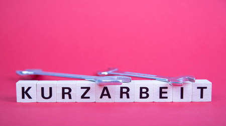 wooden blocks with german word for short time work, Kurzarbeit, above two wrenches, red backgroundの写真素材