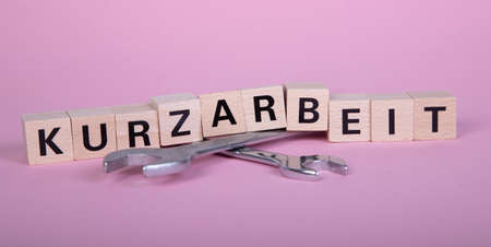 wooden blocks with german word for short time work, Kurzarbeit, above of two wrenches, pink backgroundの写真素材