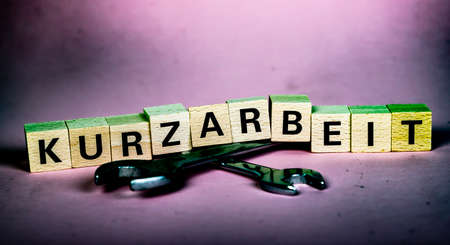 wooden blocks with german word for short time work, Kurzarbeit, above of two wrenches, pink backgroundの写真素材
