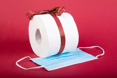 toilet paper roll with loop and a mouth protection mask as christmas present, red background