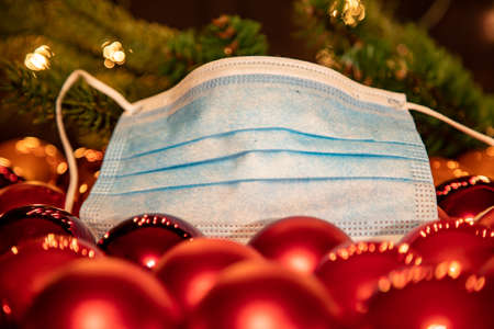 group of red christmas balls and a mouth protection mask, lights in the background. Symbol for...