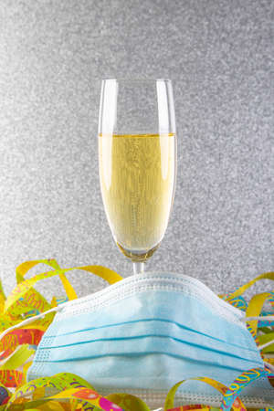 a glass of sparkling wine, a streamer as a background and a silver glitter background, face mask covering the bottom of the glas as sysbol vor impact ov Covid-19 on new year's eve 2021の写真素材