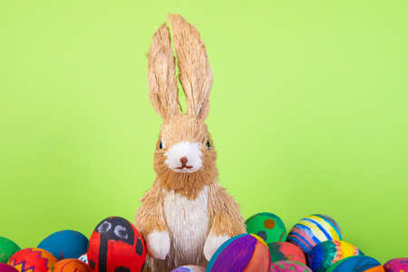 rabbit figurine between painted easter eggs before green background, easter motive