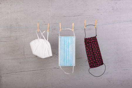 homemade face mask, ffp2 mask and a medical mask hanging on a clothesline, fixed with clothespins, white wooden board as background, which kind of mask works best to protect before corona virusの写真素材