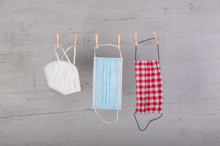 homemade face mask, ffp2 mask and a medical mask hanging on a clothesline, fixed with clothespins, white wooden board as background, which kind of mask works best to protect before corona virusの写真素材