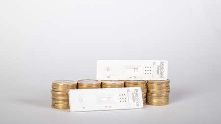 piles of one euro coins and and antigen tests as symbol for cost of testing peopleの写真素材