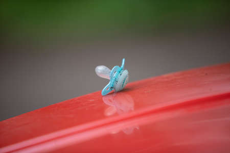 blue dirty baby pacifier on a red lid of a garbage canの写真素材