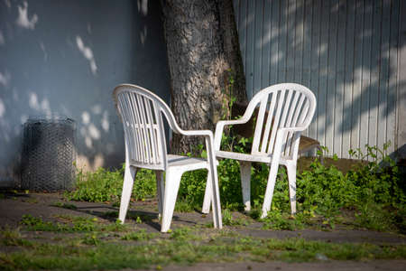 two plastic garden chairs under a treeの写真素材