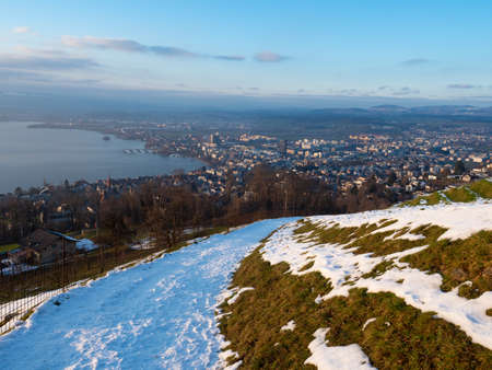 A snow-covered track leading down to the city of Zug, Switzerland, on a sunny winter afternoonの写真素材
