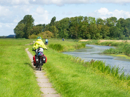 Friesland, Netherlands, August 8th 2023: Cycling on a small trail along a riverのeditorial素材