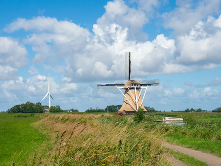 Friesland, Netherlands - August 8th 2023: A historic windmill in front of a modern wind engineのeditorial素材