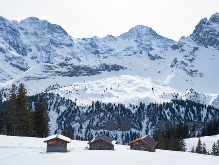 Muerren, Switzerland - February 21st 2024: Beautiful huts in the skiing resort in front of high alpine peaksの写真素材