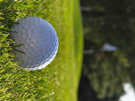 Golf ball on green grass with reflection of golf club in backgroundの写真素材
