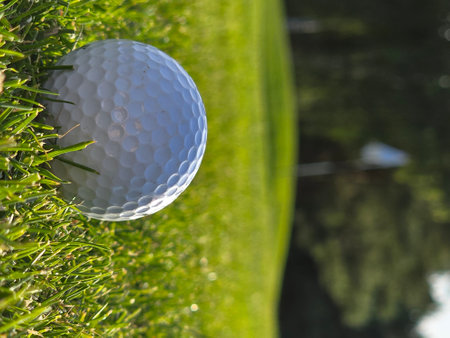 Golf ball on green grass with reflection in water, close upの写真素材
