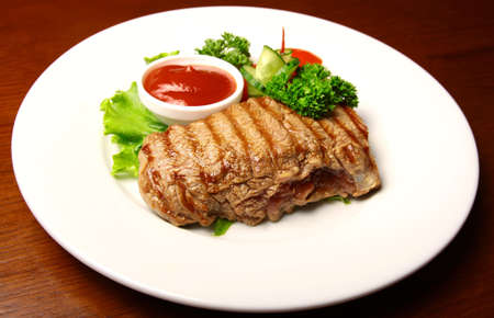 Juicy pork steak with sauce and vegetables on a plateの写真素材