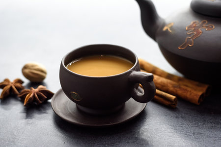 Masala tea in a clay mug and teapot. Traditional Indian hot drink with milk and spices on dark background close upの写真素材