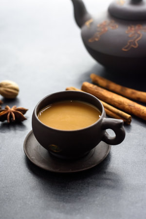 Masala tea in a clay mug and teapot. Traditional Indian hot drink with milk and spices on dark backgroundの写真素材