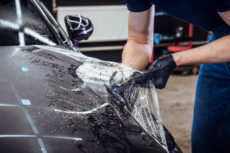 A tattooed man applies protective film to a black carの写真素材