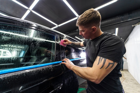 A tattooed man applies protective film to a black car