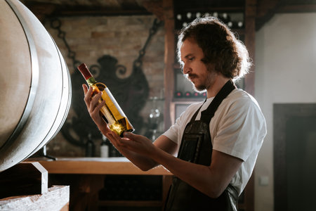 Winemaker Inspecting Bottle of White Wine in Cellar