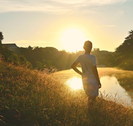 Girl in clumps of grass in the morning light and water during the morning on the river.の写真素材