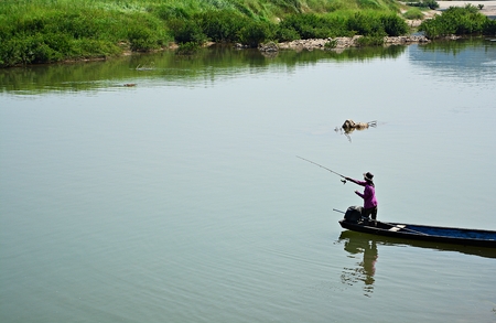 The young man was fishing on a boat in the river, a natural backdrop.の写真素材
