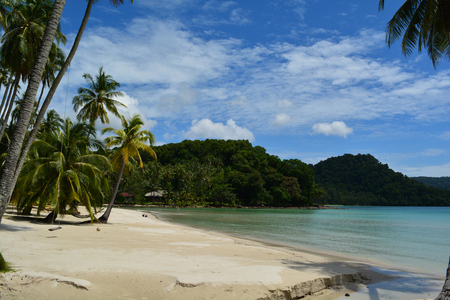 Beautiful white sand beach with coconut trees and mountains waiting for visitors.の写真素材