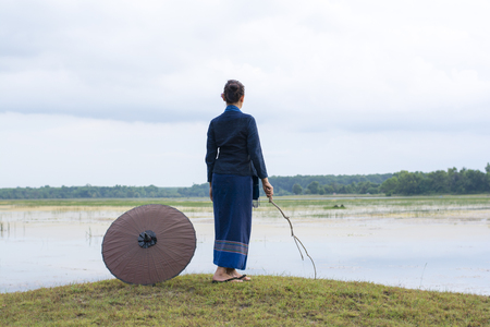Thai ladies in blue ensemble standing on the lawn looking forward to water and sky as the background.の写真素材