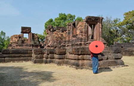 Thai woman standing in a red umbrella looking at an old temple in Thailand.の写真素材